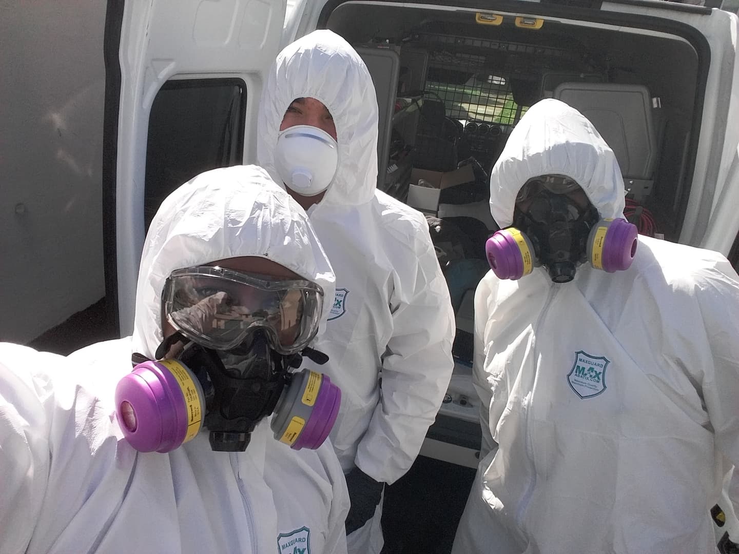 Three Mr. Fresh technicians in protective suits and respirators at the back of the work van before a job